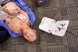 A person performing CPR on an unconscious man while a LIFEPAK CR2 AED is open and ready for use.