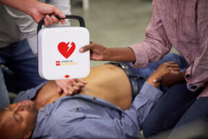 A woman receives a LIFEPAK CR2 defibrillator while performing CPR on an unconscious man.