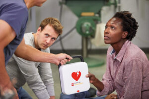 A woman receives a LIFEPAK CR2 defibrillator while performing CPR on an unconscious man.